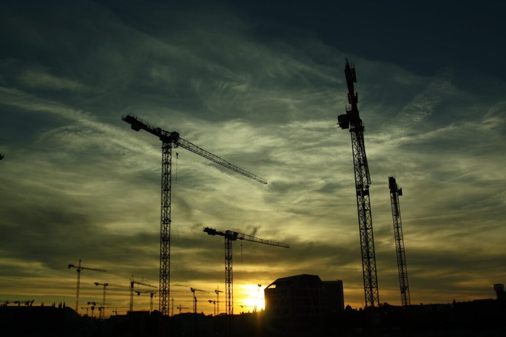 Silhouetted cranes at a construction site during sunset, showcasing industrial growth.
